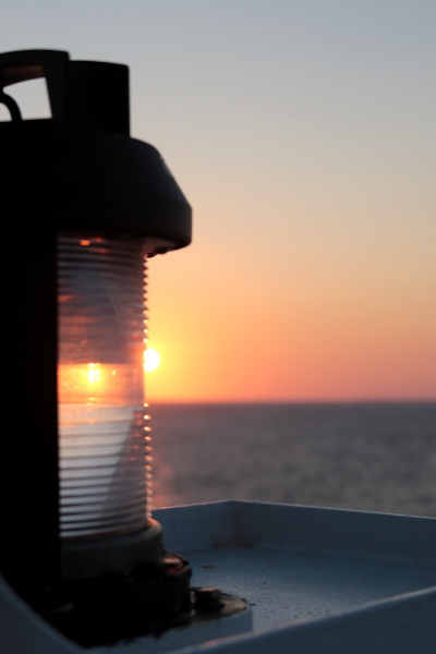 Artsy shot of the rising sun refracting through a lamp at the front of the ship.